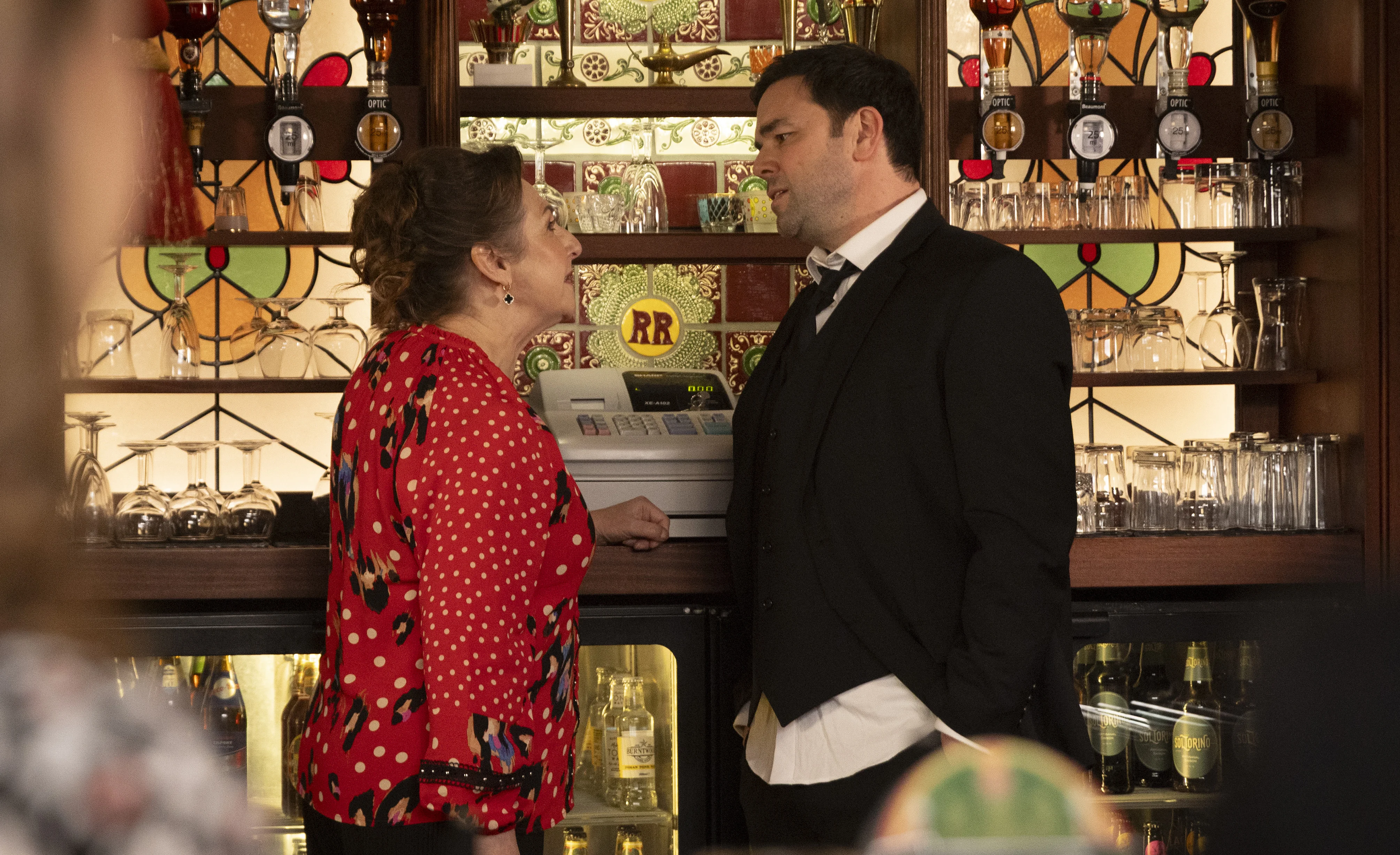Ben and Maggie Driscoll having an argument by the till behind the Rovers pub bar in Coronation Street.